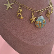 dreampunk.arts gold-tone link necklace with nautical charms, starfish, crescent moons, and a blue shell pendant.