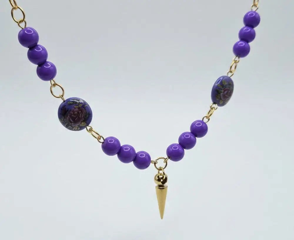 dreampunk.arts gold chain necklace with purple acrylic beads, floral glass beads, and a central gold spike pendant.